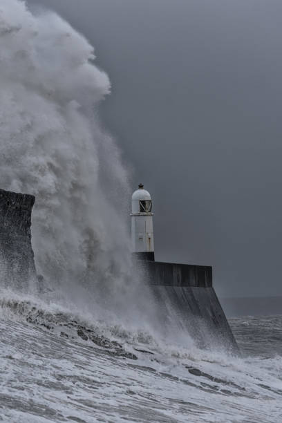 istock Huge waves breaking against a stone jetty, with a single lighthouse at the end, during a major winter storm. 1197099438