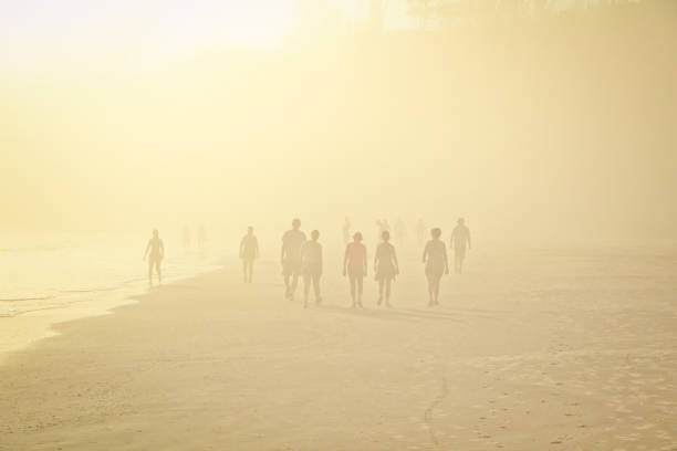 Photos of people walking on the beach in the early hours of the morning, over a slight fog