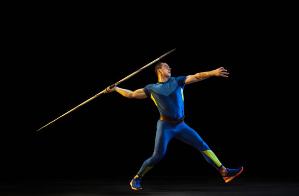 istock Male athlete practicing in throwing javelin isolated on black studio background in neon light 1197113212