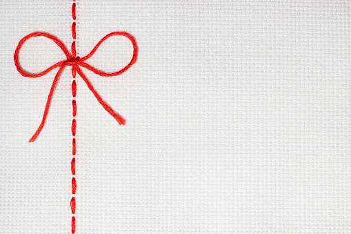 Embroidery with a red line in the form of a bow on a white fabric. Template for website design, blog, article or advertisement about cross-stitch hobby