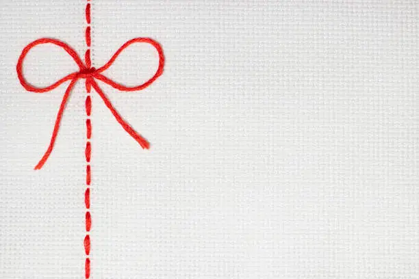 Photo of Embroidery with a red line in the form of a bow on a white fabric