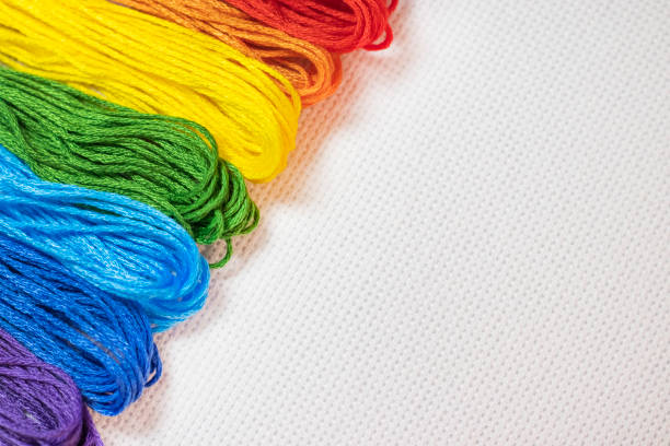 Multicolored cross stitching threads on the white textile canvas as a background. Background template with blank space for design of website , blog, article or advertisement about hobby cross stitch
