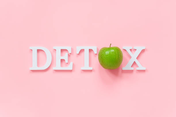 Body detoxification and healthy diet concept. Green natural fresh apple in word DETOX from white letters on pink background. Creative flat lay Top view Copy space stock photo