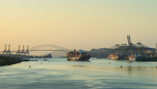 Panama Canal, Panama - December 16, 2019: Container ship enters Panama Canal at dawn. The Bridge of Americas is visible in the background.