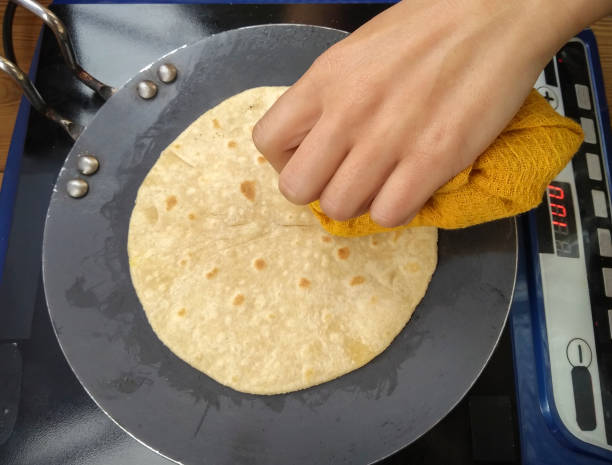 Hands making cooking chapatti on non-stick tawa in induction.