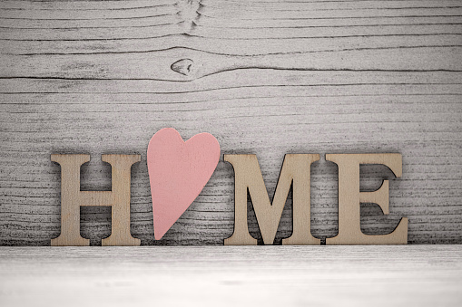 the word home in wooden letters in front of a wooden background, the O is a wooden pink heart