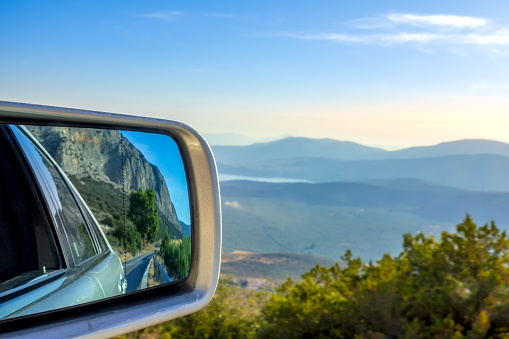 Mountain road on a summer sunny day. Panoramic view from above and a car rearview mirror