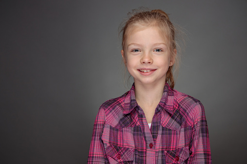 A smiling girl in purple shirt looking straight at camera. Studio shot on gray background.