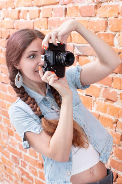 istock Vertical girl with a camera on a background of a brick wall 1197144582