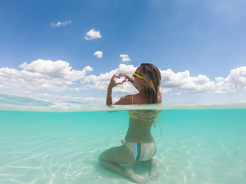 Half split underwater shot view of woman enjoying pristine clear water beach in Mexico making heart with hands