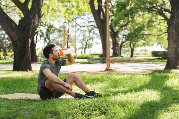 Young man drinking a protein shake in the park Young man is taking a break from his exercise to make and drink a nutritional protein shake. protein stock pictures, royalty-free photos & images