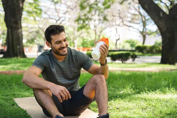 Young man is taking a break from his exercise to make and drink a nutritional protein shake.