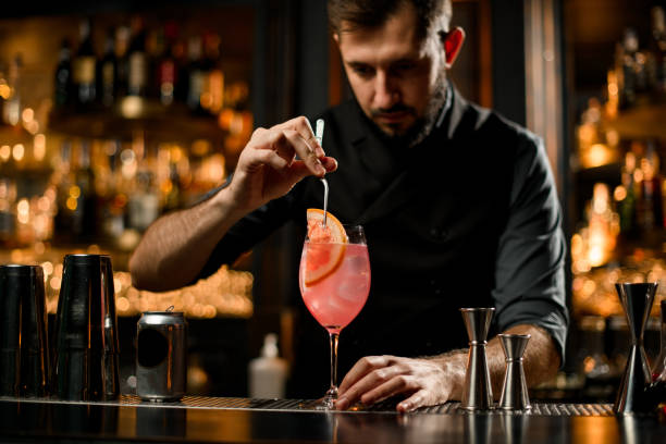 istock Bartender decorated the pink color alcoholic cocktail drink with a grapefruit slice with tweezers 1197152997