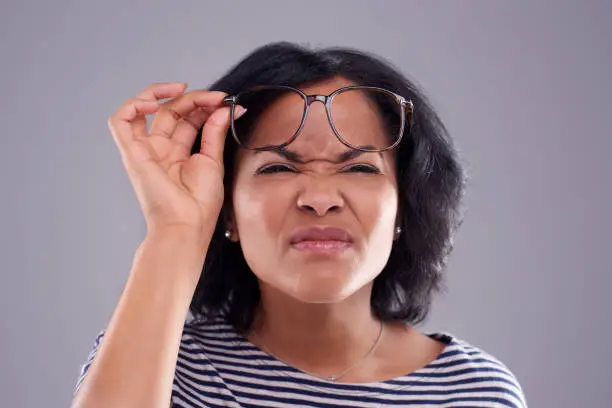 Studio shot of a woman struggling to see without her glasses against a grey background