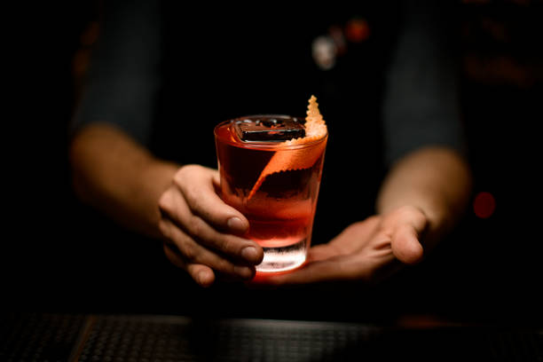 male bartender serving the red alcoholic drink decorated with the spiral orange zest and ice - drink on top of ice food imagens e fotografias de stock