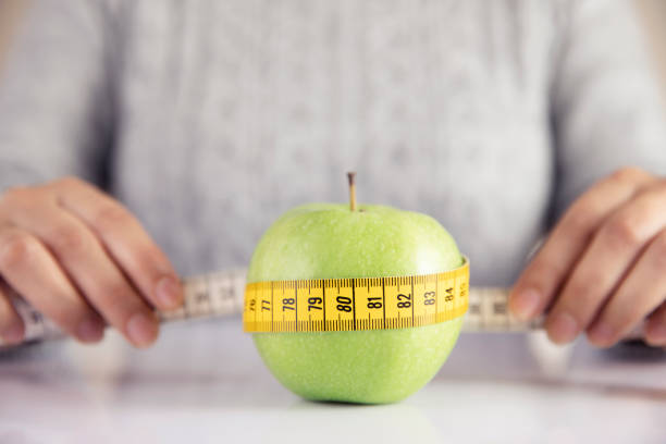 Young woman holding a tape measure on green apple to show eating healthy