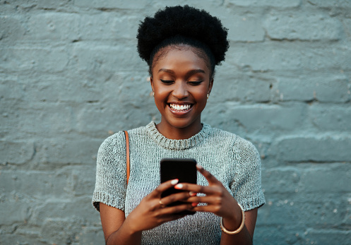 Shot of an attractive young creative businesswoman using her cellphone while standing against a grey wall outdoors