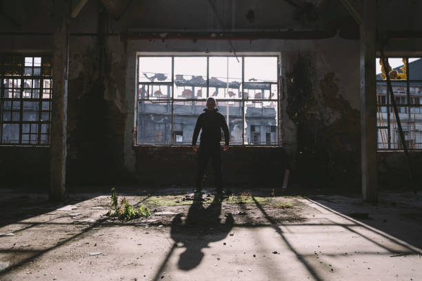 istock Adult man standing inside some large, dark, spooky,abandoned building illuminated with sunlight through window 1197158329
