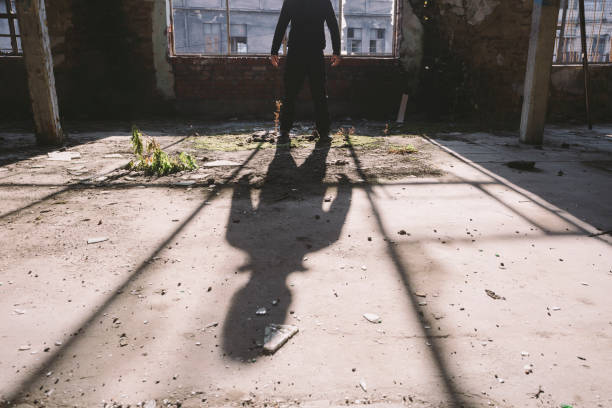 istock Adult man standing inside some large, dark, spooky,abandoned building illuminated with sunlight through window 1197158365