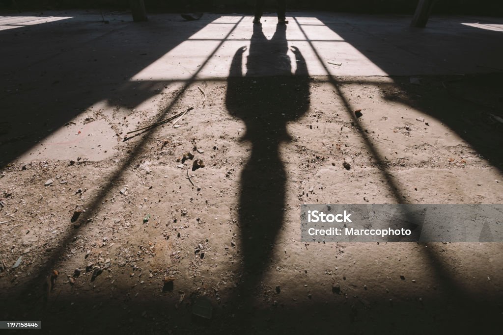 Adult man standing inside some large, dark, spooky,abandoned building illuminated with sunlight through window Photo is taken with full frame dslr camera indoors. Serial Killings Stock Photo