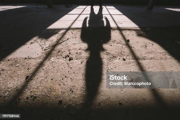 Adult Man Standing Inside Some Large Dark Spookyabandoned Building Illuminated With Sunlight Through Window Stock Photo - Download Image Now