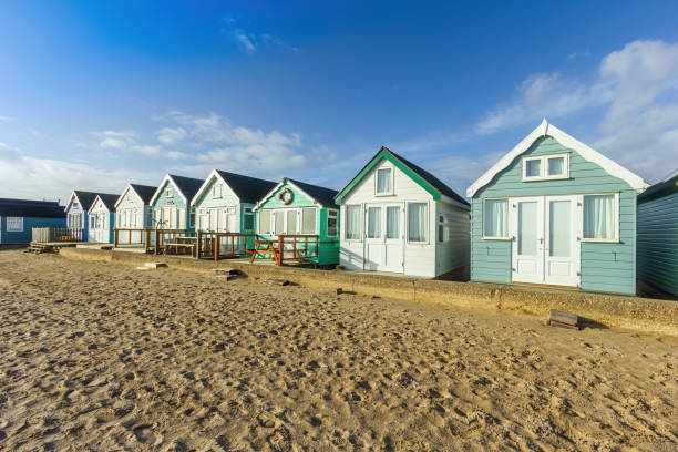 A close up view of colorful beach huts with a sandy beach in the foreground under a majestic blue sky and some white clouds A close up view of colorful beach huts with a sandy beach in the foreground under a majestic blue sky and some white clouds hengistbury head photos stock pictures, royalty-free photos & images