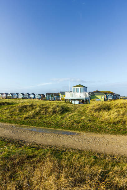 A view of colorful beach huts with a lifeguard post, track and grass in the foreground under a majestic blue sky and some white clouds A view of colorful beach huts with a lifeguard post, track and grass in the foreground under a majestic blue sky and some white clouds hengistbury head photos stock pictures, royalty-free photos & images