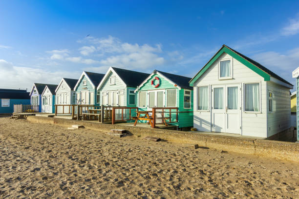 A close up view of colorful beach huts with a sandy beach in the foreground under a majestic blue sky and some white clouds A close up view of colorful beach huts with a sandy beach in the foreground under a majestic blue sky and some white clouds hengistbury head photos stock pictures, royalty-free photos & images