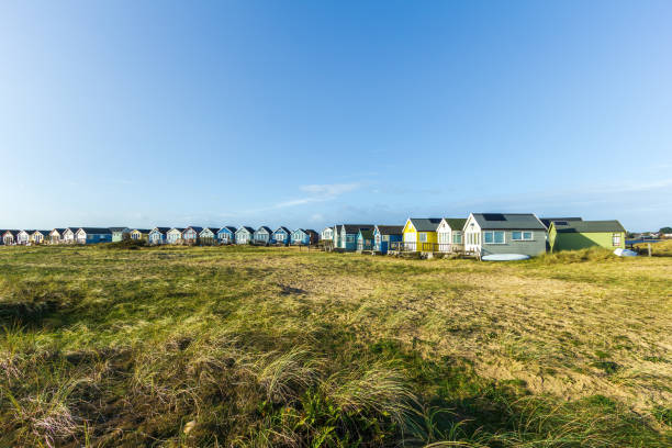 A view of colorful beach huts with a sandy beach and grass in the foreground under a majestic blue sky and some white clouds A view of colorful beach huts with a sandy beach and grass in the foreground under a majestic blue sky and some white clouds hengistbury head photos stock pictures, royalty-free photos & images