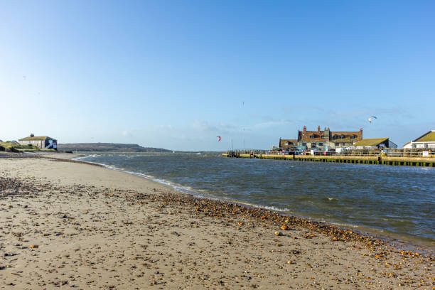 A view of a water channel between Christchurch (UK) harbor and bay with sandy beach and fishering buildings along the banks under a majestic blue sky A view of a water channel between Christchurch (UK) harbor and bay with sandy beach and fishering buildings along the banks under a majestic blue sky hengistbury head photos stock pictures, royalty-free photos & images