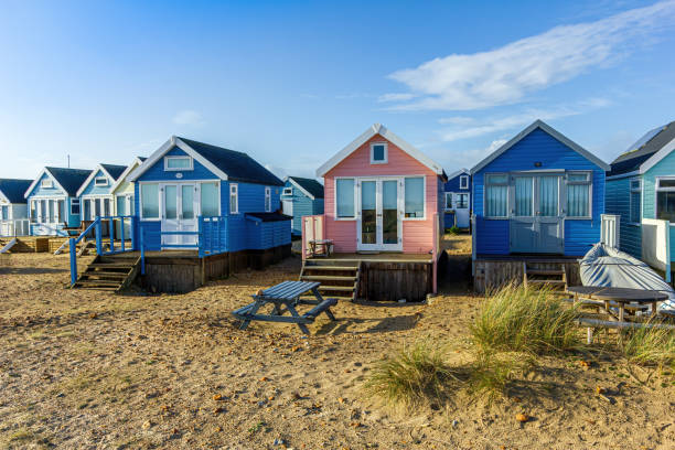 A close up view of colorful beach huts with a sandy beach and grass in the foreground under a majestic blue sky and some white clouds A close up view of colorful beach huts with a sandy beach and grass in the foreground under a majestic blue sky and some white clouds hengistbury head photos stock pictures, royalty-free photos & images