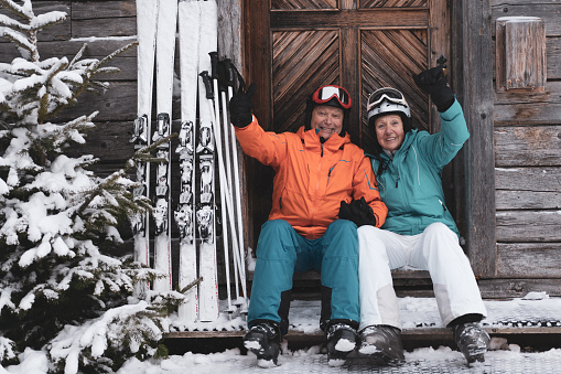 cheerful seniors skier couple sitting at wooden mountain lodge hut smiling at camera on cold winter day