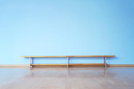 wide laminate floor and huge empty blue wall in empty room with wooden bench