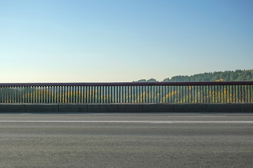 road over the bridge with railings, protection from accidents, autumn landscape and blue sky background