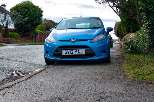 A car parks on the pavement / sidewalk, severely restricting space for pedestrians - taken in the UK.