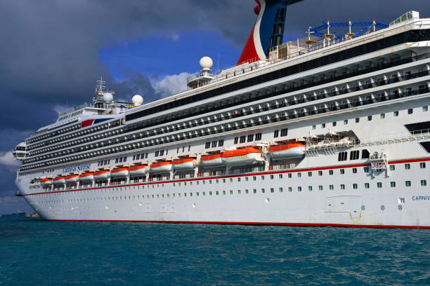 Ocho Rios, Jamaica - December 30, 2019: Fisherman standing on a small boat with fishing rods in the foreground, with the Carnival Victory cruise ship docked in the background and clear blue Caribbean waters