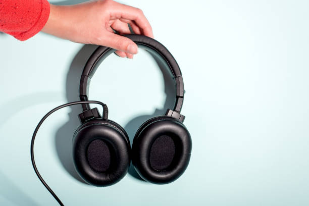 istock Black massive headphones in female hand on pastel background, copy space. Modern technology flat lay with over-ear earphones in woman hand, modern lifestyle concept 1197175562