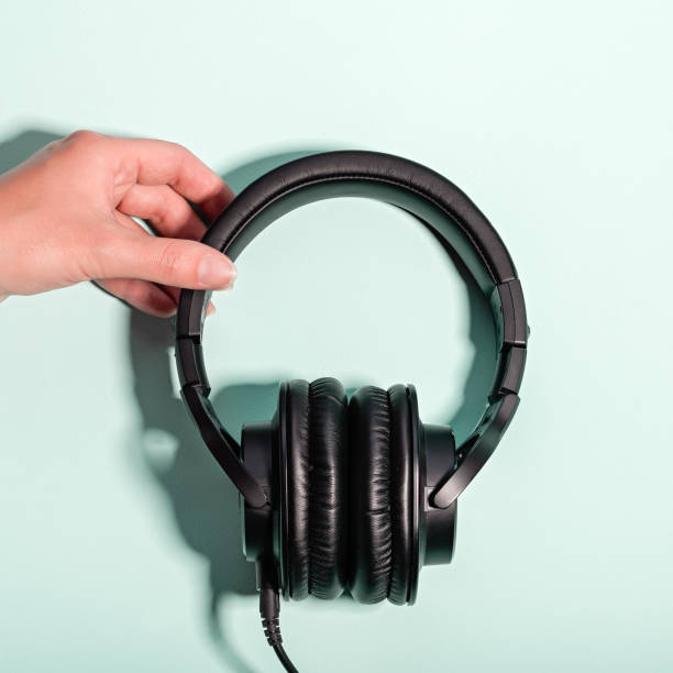 istock Black massive headphones in female hand on pastel background, copy space. Modern technology flat lay with over-ear earphones in woman hand, modern lifestyle concept 1197175565