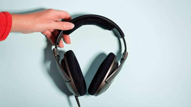 istock Black massive headphones in female hand on pastel background, copy space. Modern technology flat lay with over-ear earphones in woman hand, modern lifestyle concept 1197175569