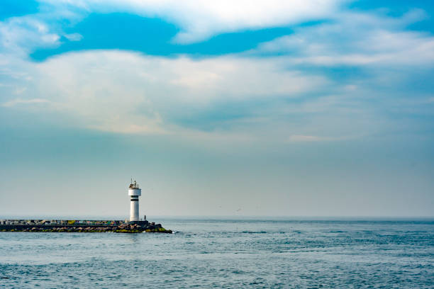 In cloudy day, a man standing near the small lighthouse alone.