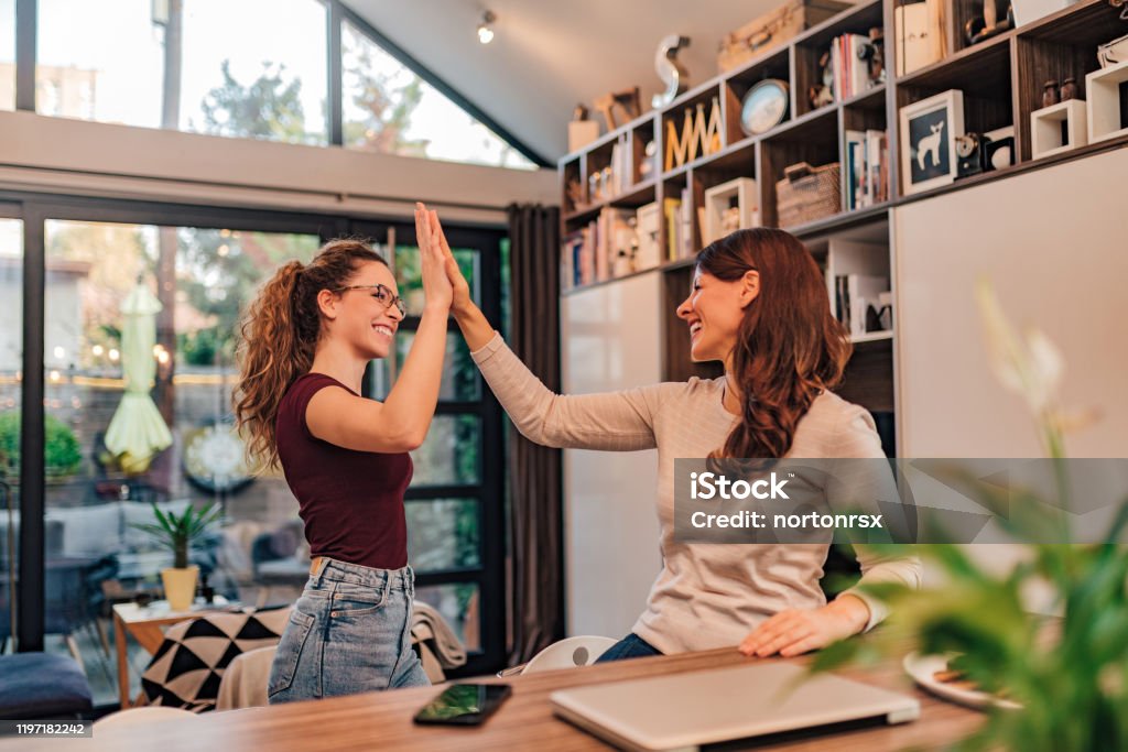 Two cheerful women high five at cozy modern house. Entrepreneur Stock Photo