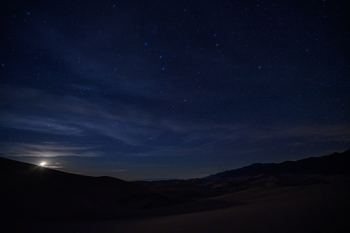 Moon Sets Below Sand Dunes and Star Field on mostly clear night