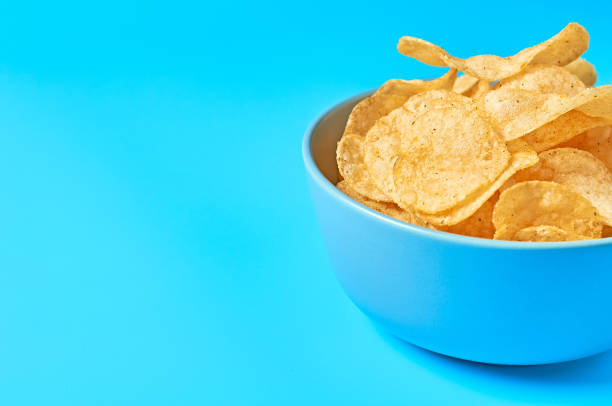 istock Full ceramic bowl of potato chips on blue background. Space for text 1197184616