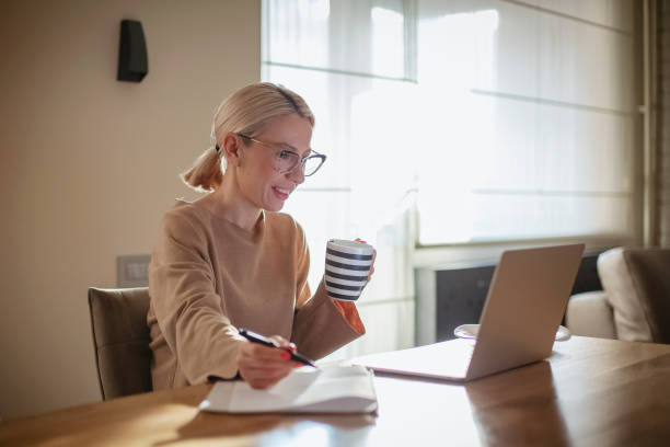 woman working at home while having breakfast - furniture internet adult blond hair imagens e fotografias de stock