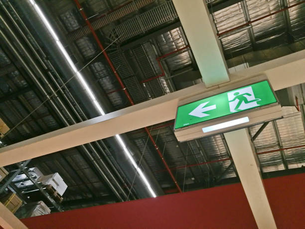 segnale del percorso di uscita di emergenza in cima al magazzino di fabbrica - direction arrow sign road sign escape foto e immagini stock