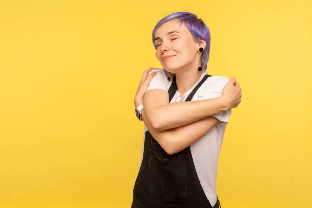 portrait of beautiful hipster girl embracing herself and smiling from happiness and pleasure. yellow background, studio shot - urgency body care young adult people imagens e fotografias de stock