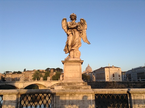 Sunlit angel statue on Rome bridge