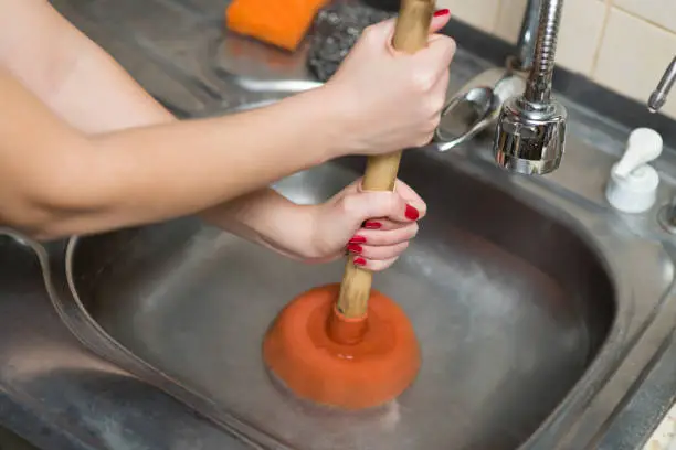 female hands apply plunger to the kitchen sink, no face