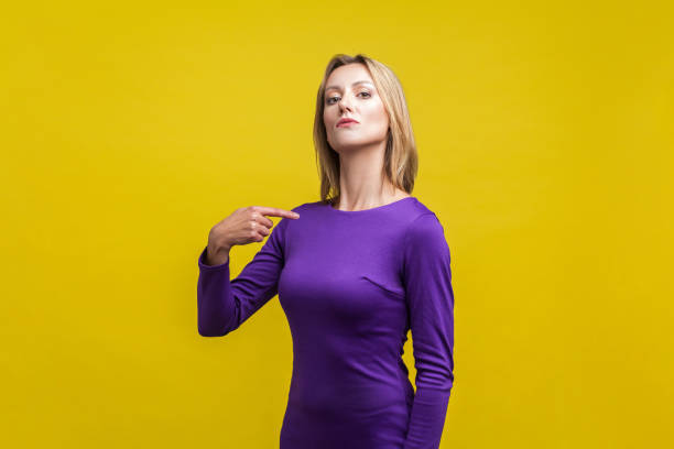 this is me! portrait of arrogant businesswoman pointing at herself. indoor studio shot isolated on yellow background - smug imagens e fotografias de stock