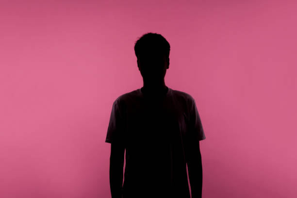 Anonymous person. Silhouette portrait of young man in casual T-shirt isolated on pink background No name, anonymous person hiding face in shadow, human identity. Silhouette portrait of young man in casual T-shirt standing calm with hands down, indoor studio shot, isolated on pink background person shadow stock pictures, royalty-free photos & images